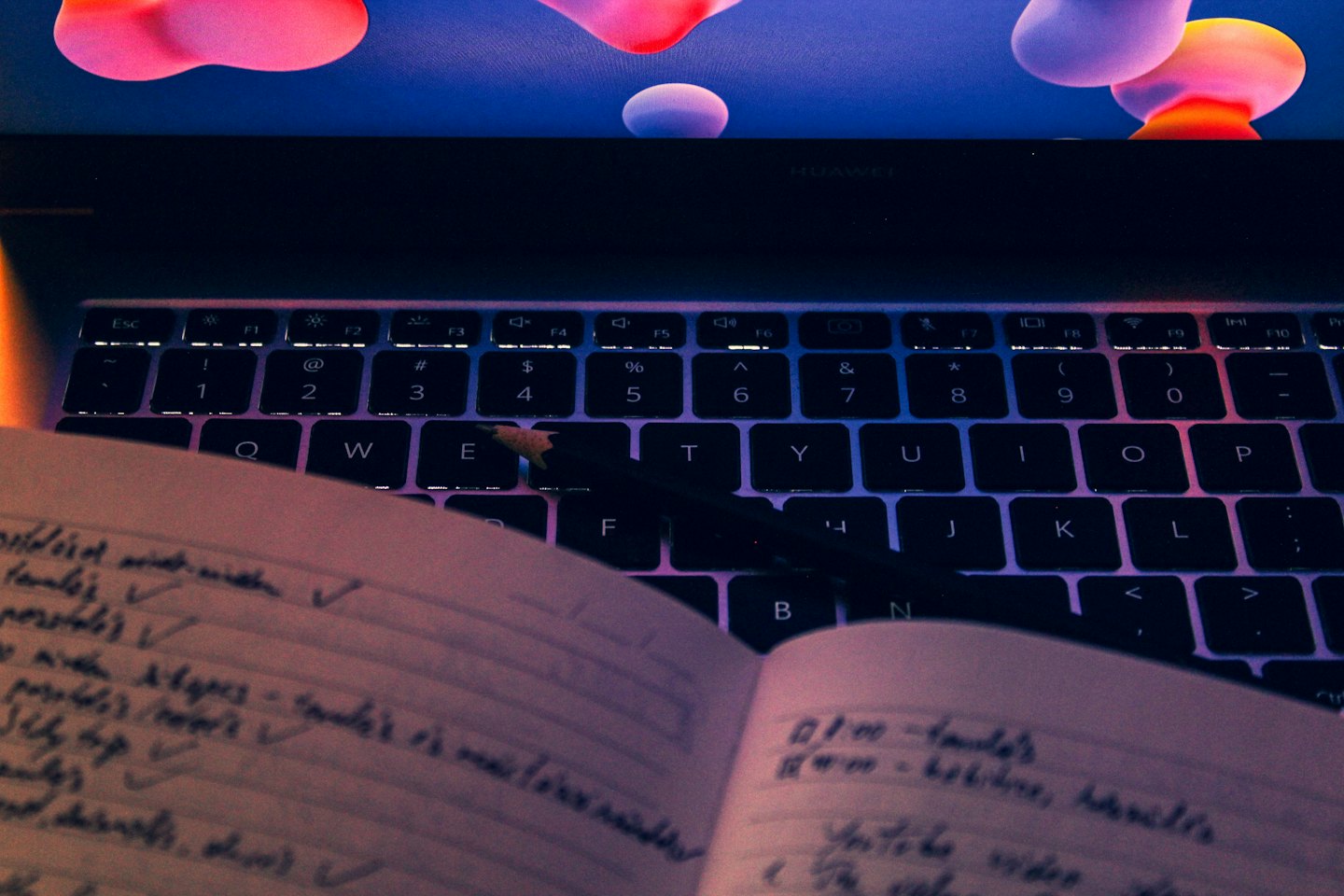Laptop keyboard and open notebook sit on a desk.